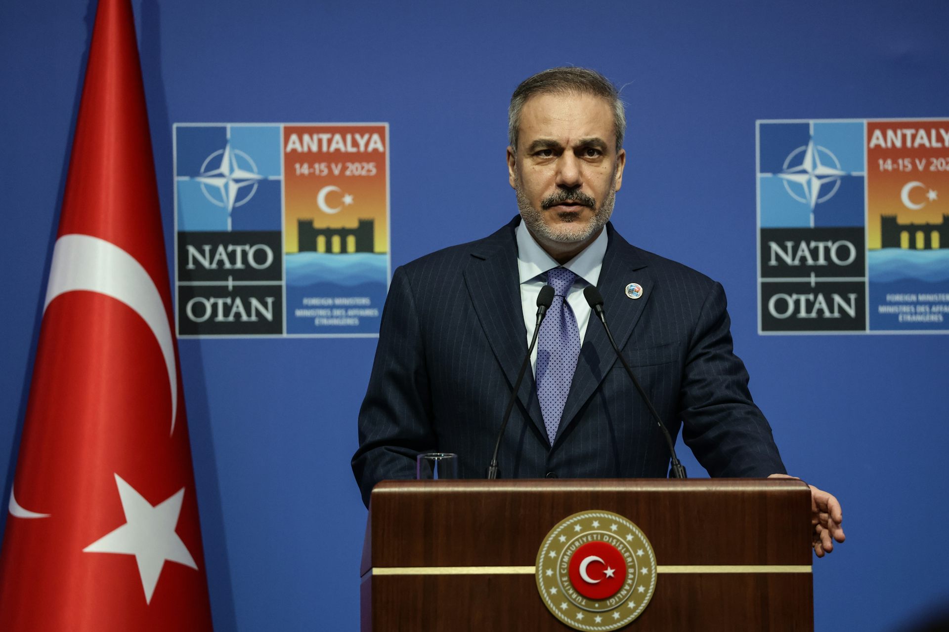 Turkey's foreign minister Hakan Fidan stands at a lectern in front of a Turkish flag and Nato posters.
