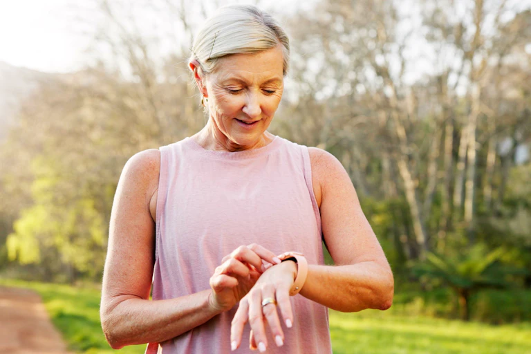 An older woman checks her smartwatch while on a walk outdoors.