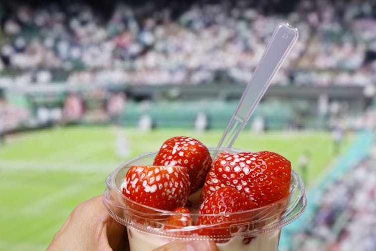 dish of cream and strawberries at Wimbledon with the court in the background.