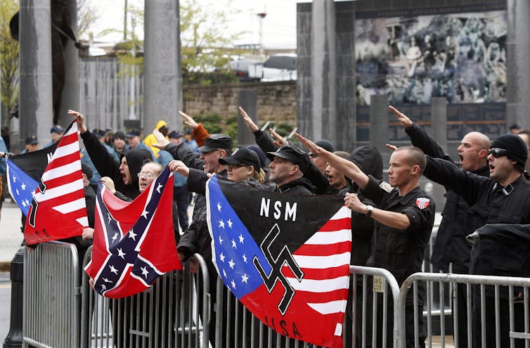 Men and women standing behind a barricade, holding flags with swastika signs on them.