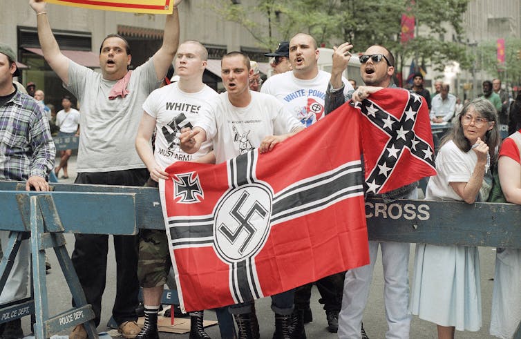 Men standing behind a barricade, holding a red flag with a swastika sign on it.