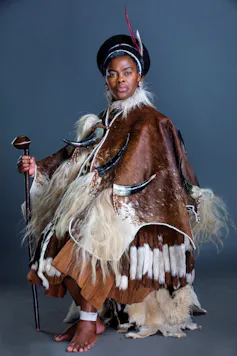 An African woman poses proudly in an elaborate traditional outfit of animal hide.