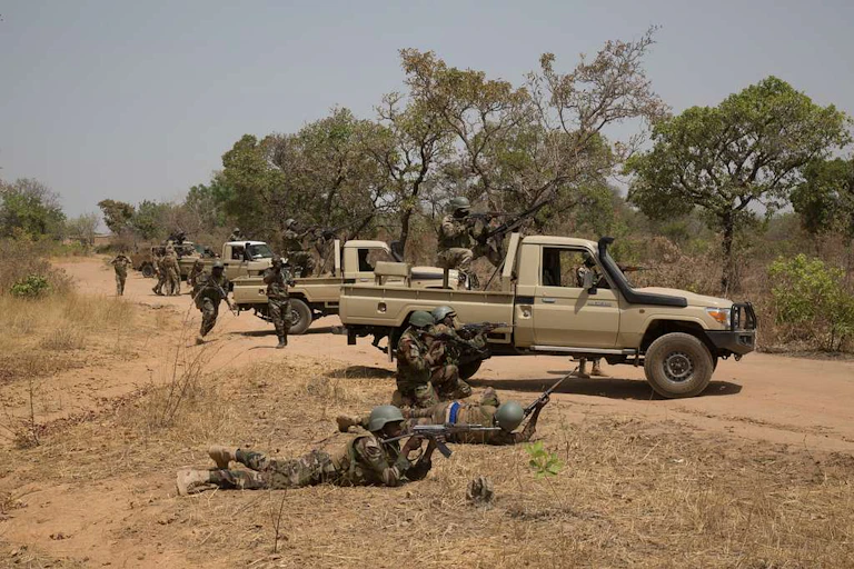 Vehicles parked on an unpaved roads, with soldiers in uniform in and around them