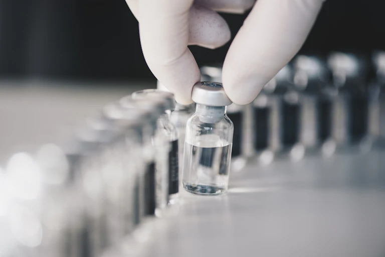 Gloved fingers pick up a vial out of a line of vials in a scientific experiment.