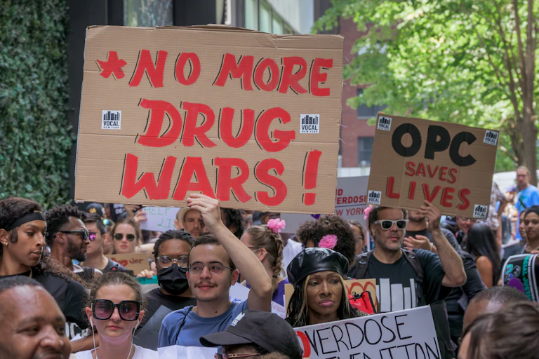 People march down a street on a sunny day holding signs calling for an end to the War on Drugs.