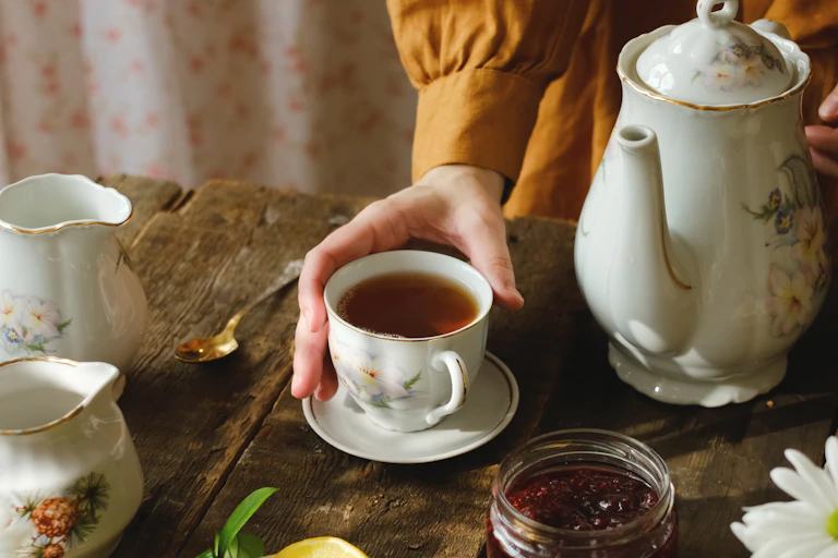 Hand holding cup of black tea on wooden served table.