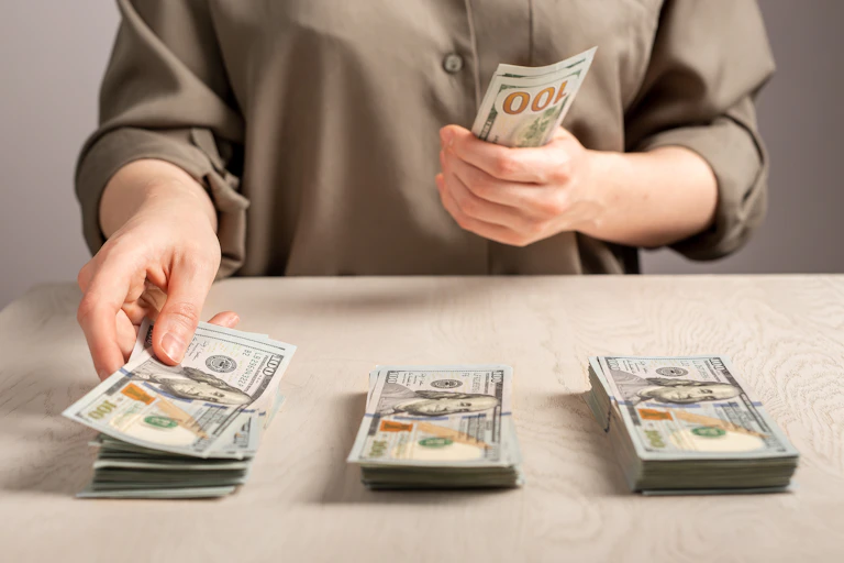 A person holds a stack of money and sorts it into three piles.