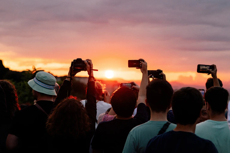 A crowd of people taking photos of a vibrant sunset on their smartphones.