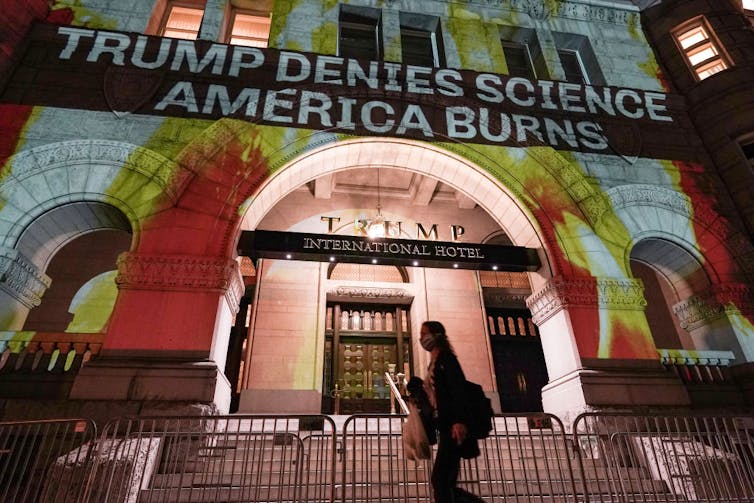 People walk by a projection of flames and commentary on the side of the Trump International Hotel