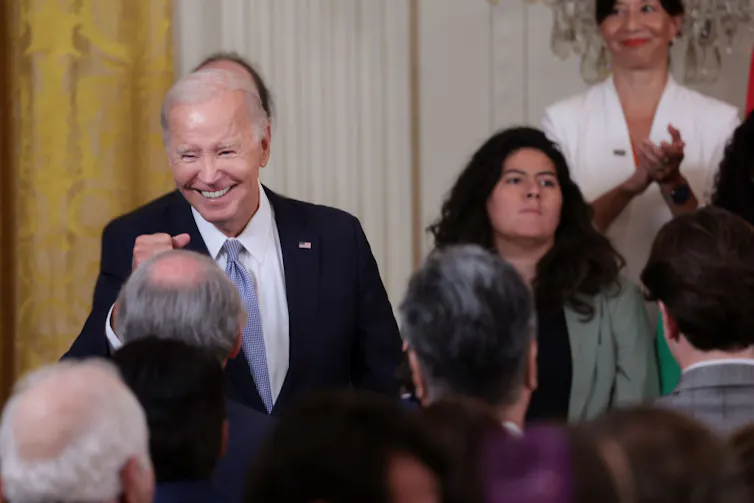 a man wearing a suit smiles in front of small crowd