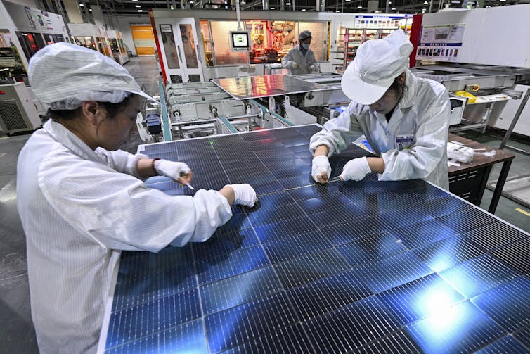 Two workers wearing white clothes working on a solar panel.