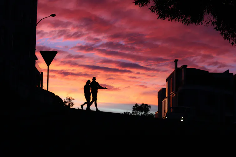 Two people walking on a city street silhouetted against a red sky.