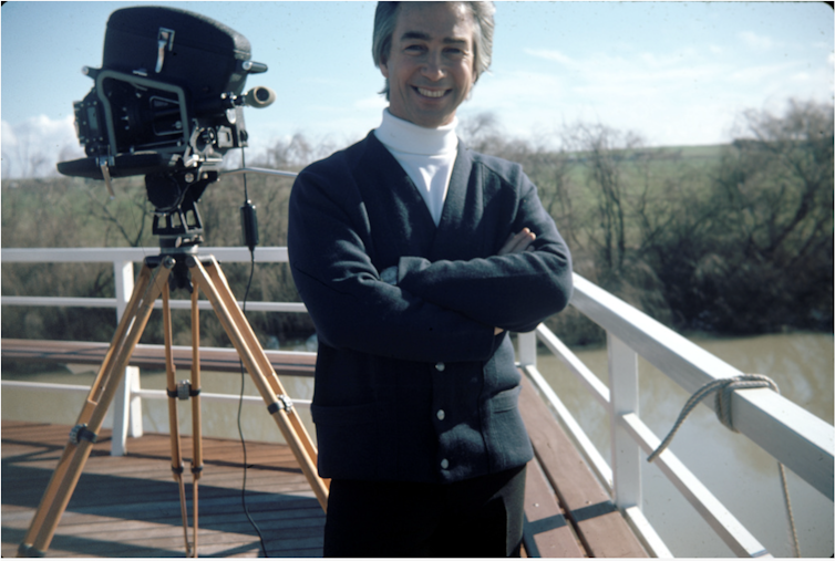 Dunstan stands next to a film camera.
