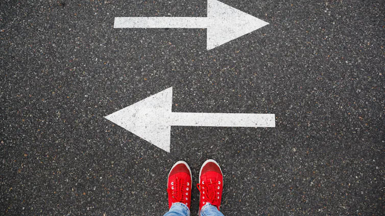 feet in red sneakers stand on road with white painted arrows pointed to left and to right