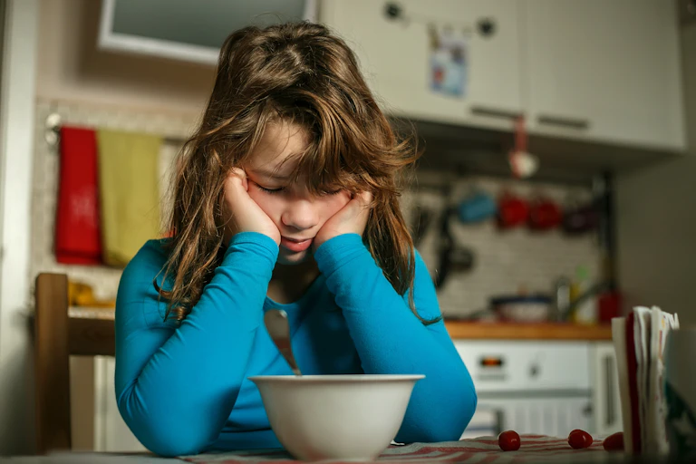 Girl looking sad at breakfast table with bowl
