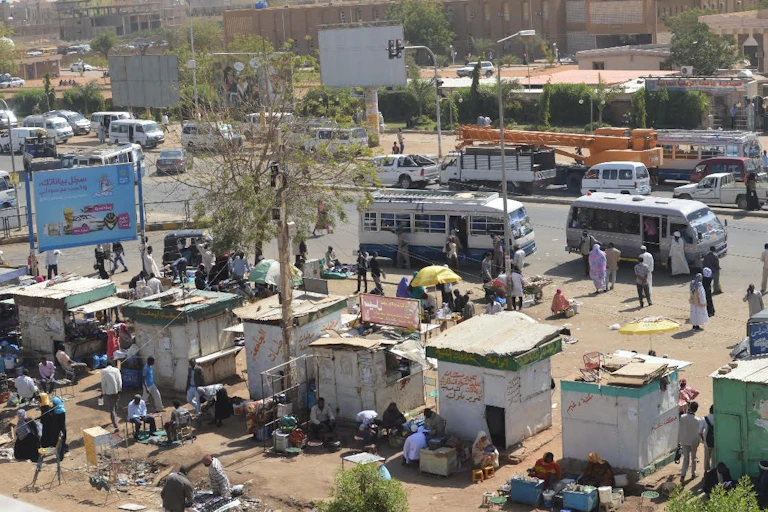 People mill around several small shanties made with metal sheets