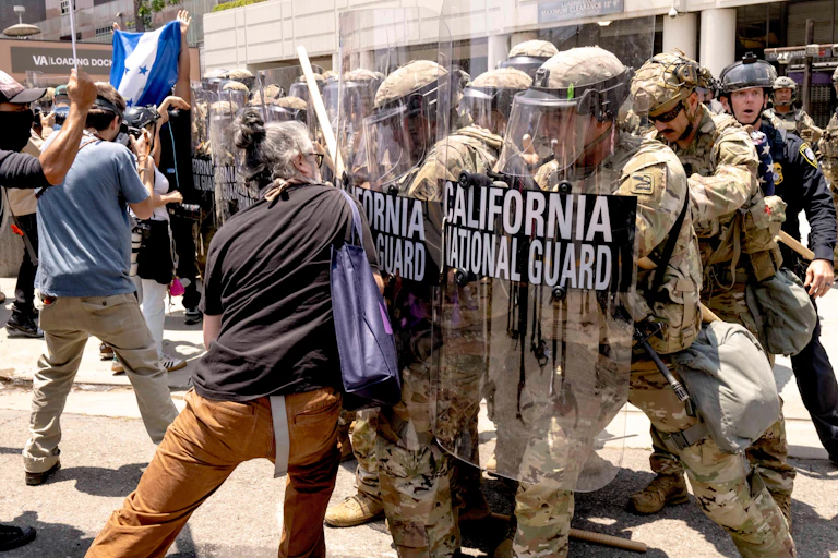 A protester pushes against a national guard with a shield.