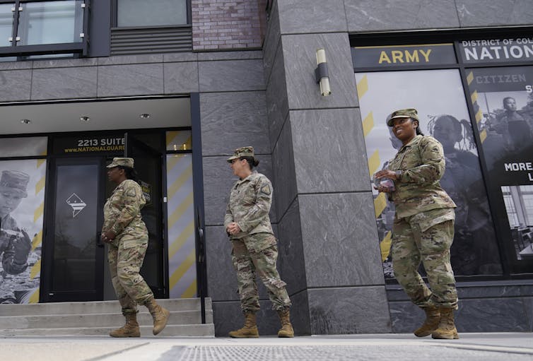 Three women dressed in U.S. military gear stand outside a building.