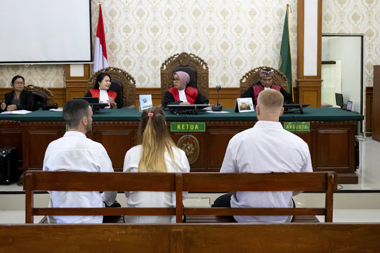 View from behind of three people in white shirts, sitting side by side in a courtroom