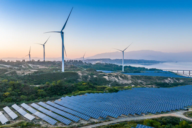 Rolling hills with giant sets of solar panels in lines of about 30 and several big wind turbines dotted over them