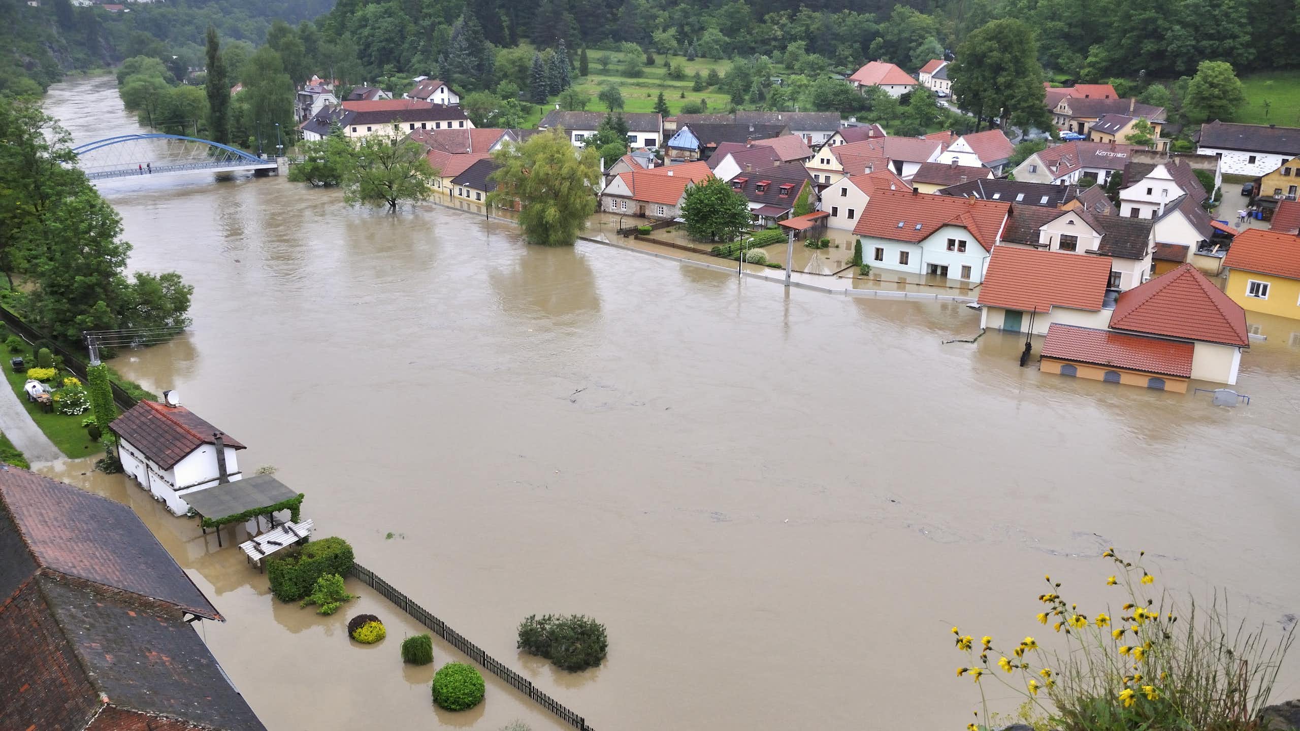 A river with brown water has partially flooded some nearby buildings.