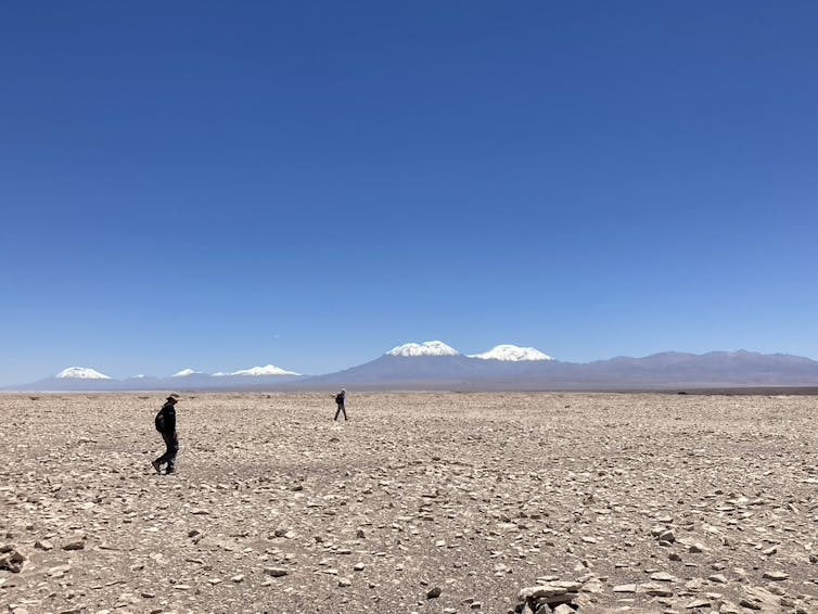 Dos personas caminando por la superficie rocosa del desierto de Atacama