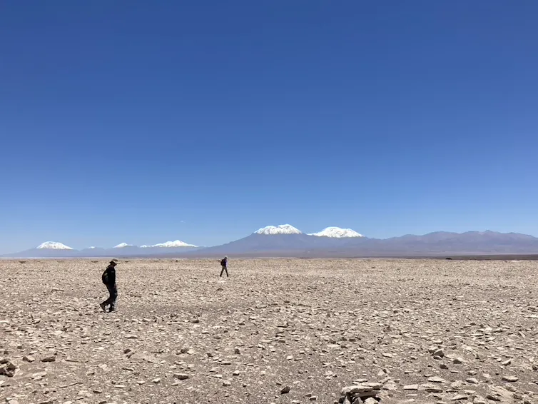 Dos personas caminando por la superficie rocosa del desierto de Atacama