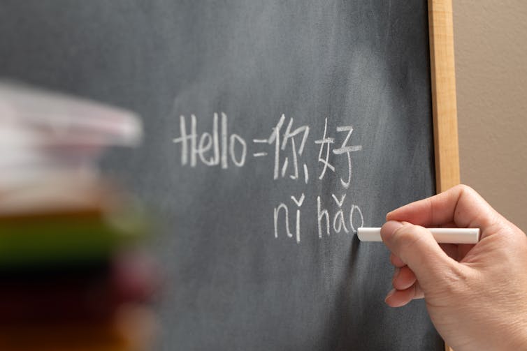 A student holding chalks writes Mandarin text on a blackboard.