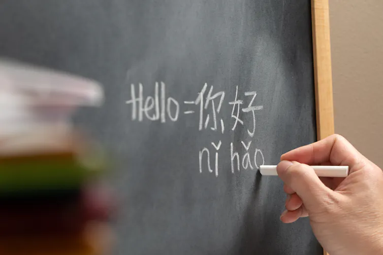 A student holding chalks writes Mandarin text on a blackboard.