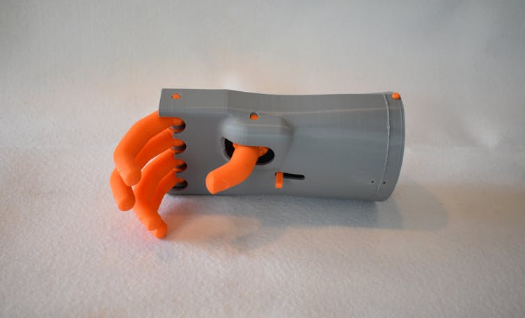 Mano mecánica con dedos de plástico de naranja que se extiende desde una palma gris plástica y muñeca