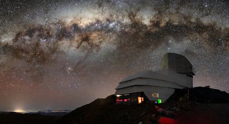 An observatory, which looks like a building with a dome atop it, on a mountainside, with a starry sky shown in the background.