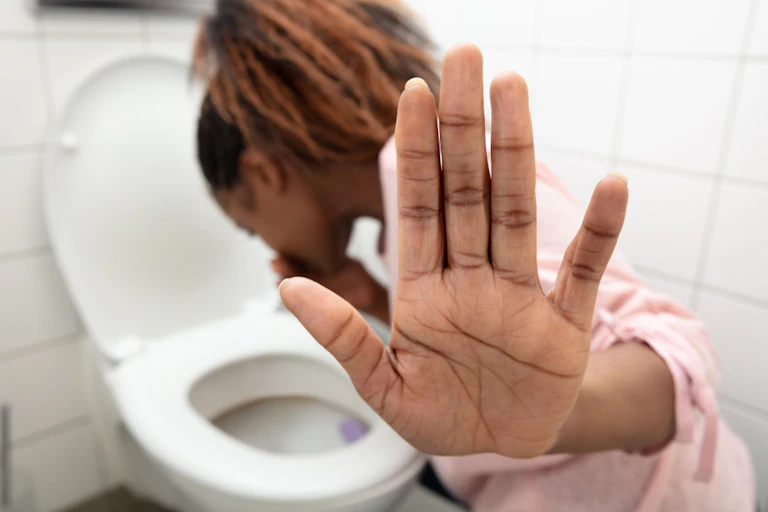 Woman holding palm to camera while vomiting in toilet