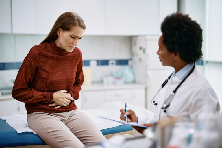 A woman with abdominal pain speaks with her female doctor about her concerns in the doctor's examination room.