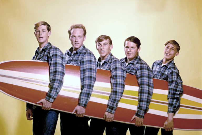 Cinco chicos sosteniendo una tabla de surf.