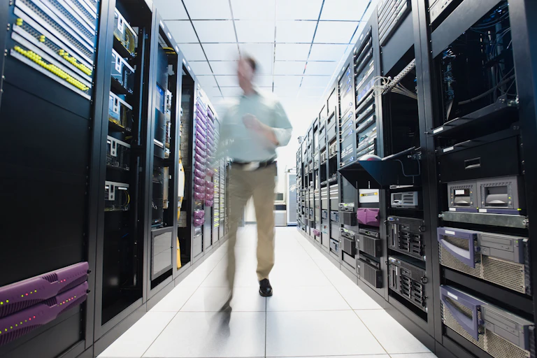 A blurred person walking between rows of stacked servers in a datacentre.