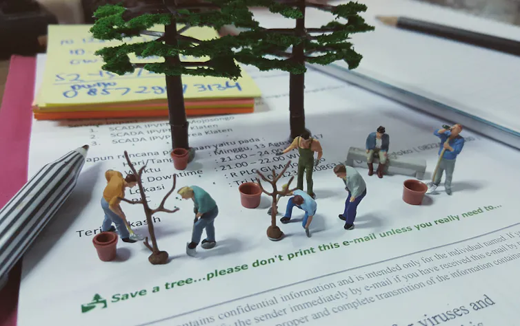 Plastic figures plant trees on top of paper saying 'please don't print'