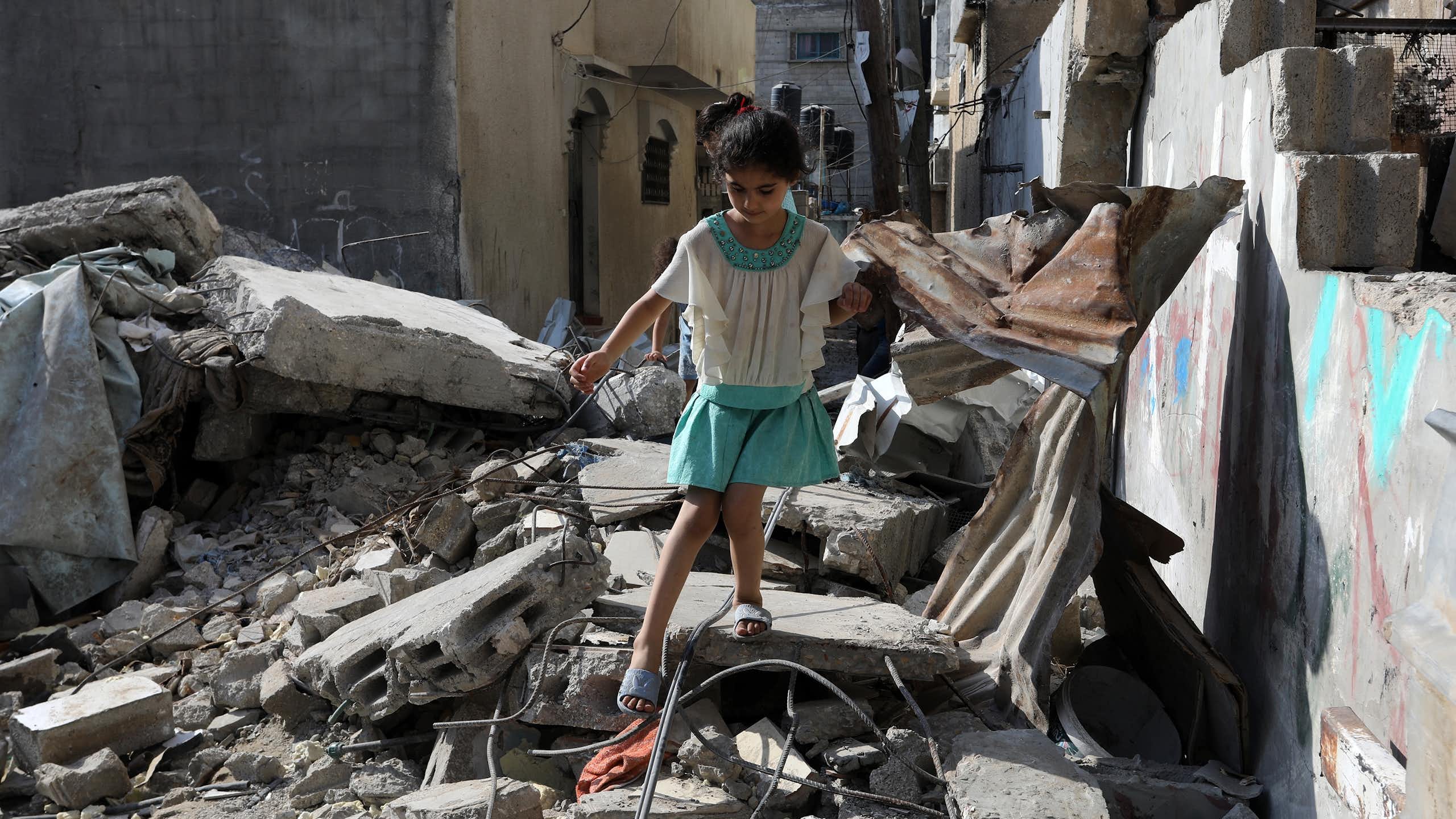 Une petite fille marche prudemment sur des gravats, dans une zone de conflit
