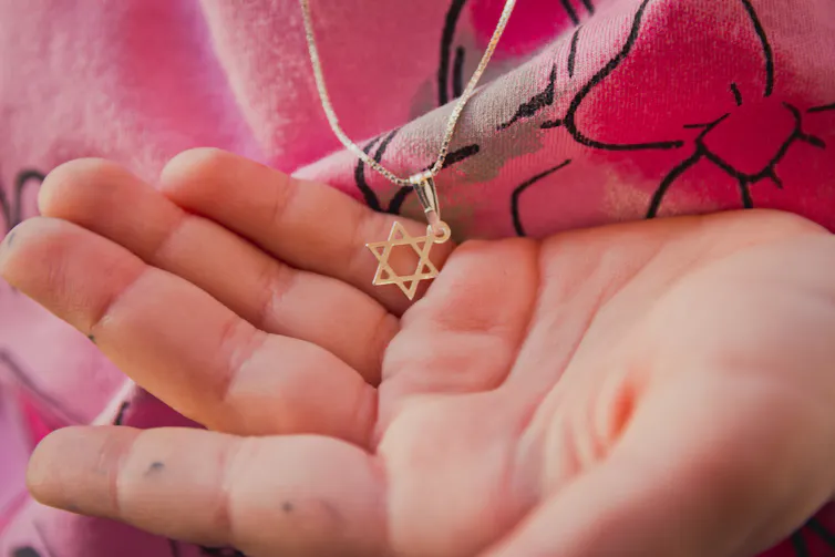 Someone wearing a pink shirt cups a small necklace with a six-pointed star in their hand.