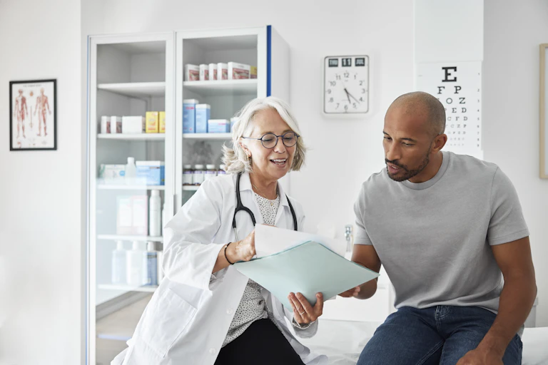 Female doctor reviews test results with a male patient at health clinic examination room.