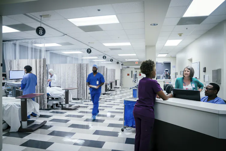 People in scrubs work and mill about in a hospital emergency room.