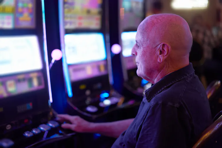 Older man playing on slot machine.