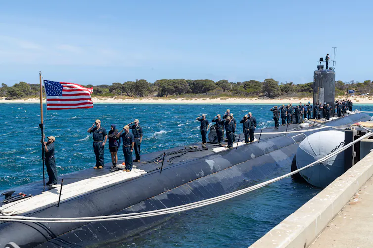 Sailors assigned to the Los Angeles-class fast-attack submarine USS Asheville (SSN 758) salute the national ensign after arriving at Royal Australian Navy HMAS Stirling Naval Base.