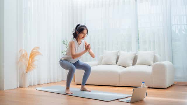 Una mujer hace sentadillas frente a un ordenador portátil