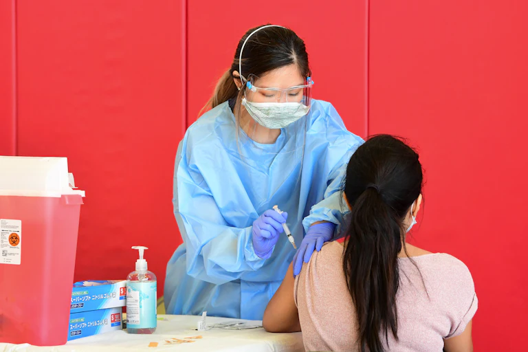 A nurse in a face mask administers a COVID-19 vaccine to a woman.