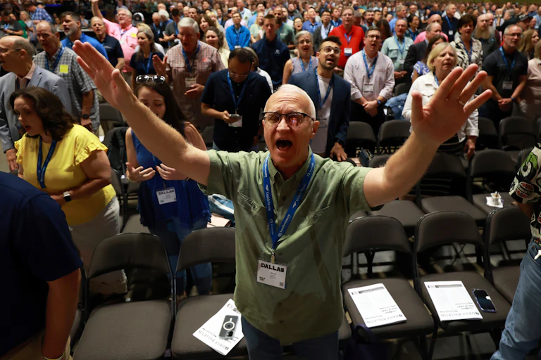 A man, standing amid a large group of people, raises both his hands.