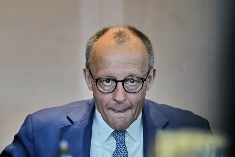 A balding white man with dark glasses wearing a blue suit