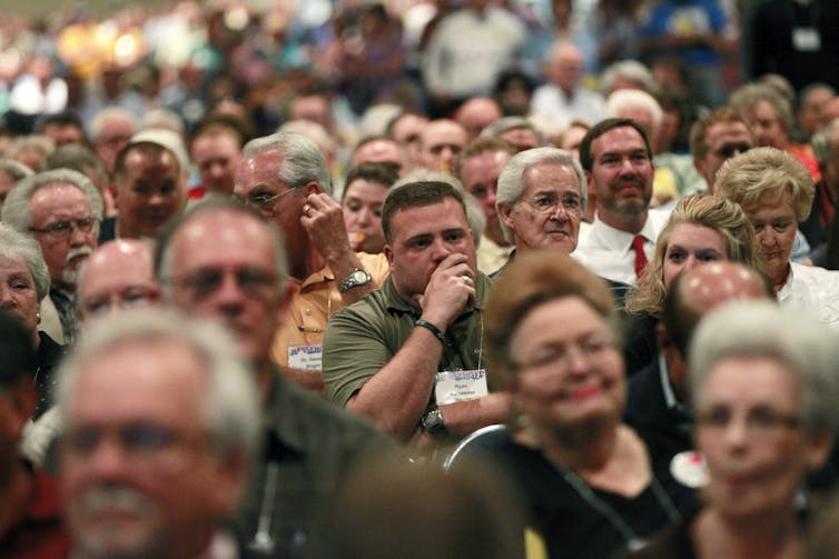 Close-up of several seated individuals looking ahead while listening to a speaker, with a few seen smiling.