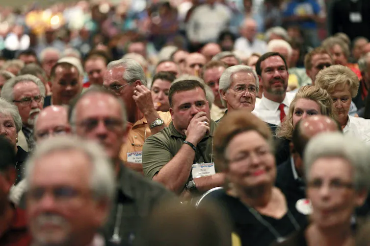 Close-up of several seated individuals looking ahead while listening to a speaker, with a few seen smiling.