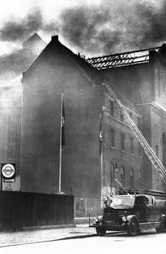 A black and white photo of a building on fire with a fire truck parked next to it