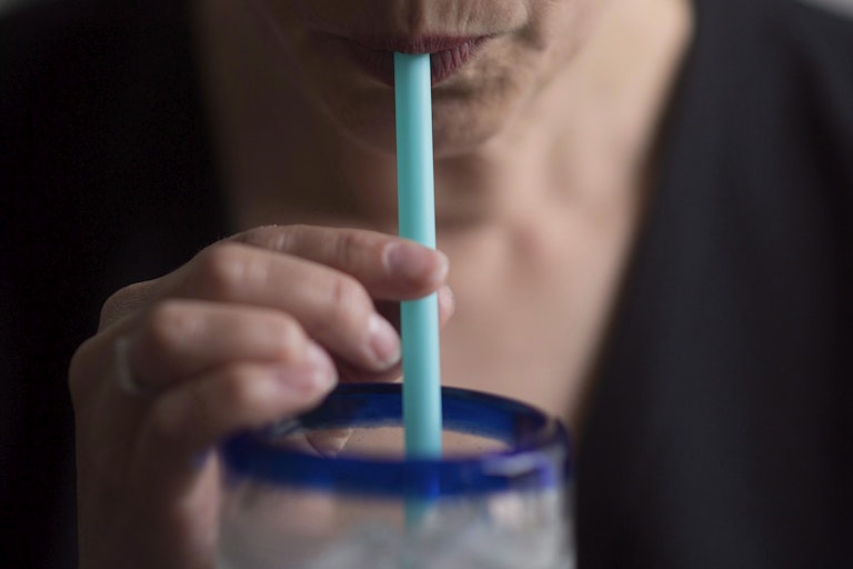 Close up of someone's mouth drinking through a plastic strawn